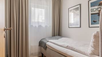 A bedroom with a bed, a window with sheer curtains, and two framed pictures on the wall.