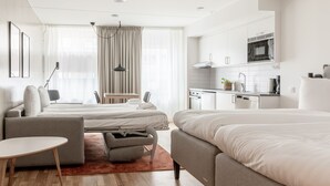 Een moderne hotelkamer met twee bedden, een klein zitehoekje, een kitchenette en een groot raam met gordijnen.
