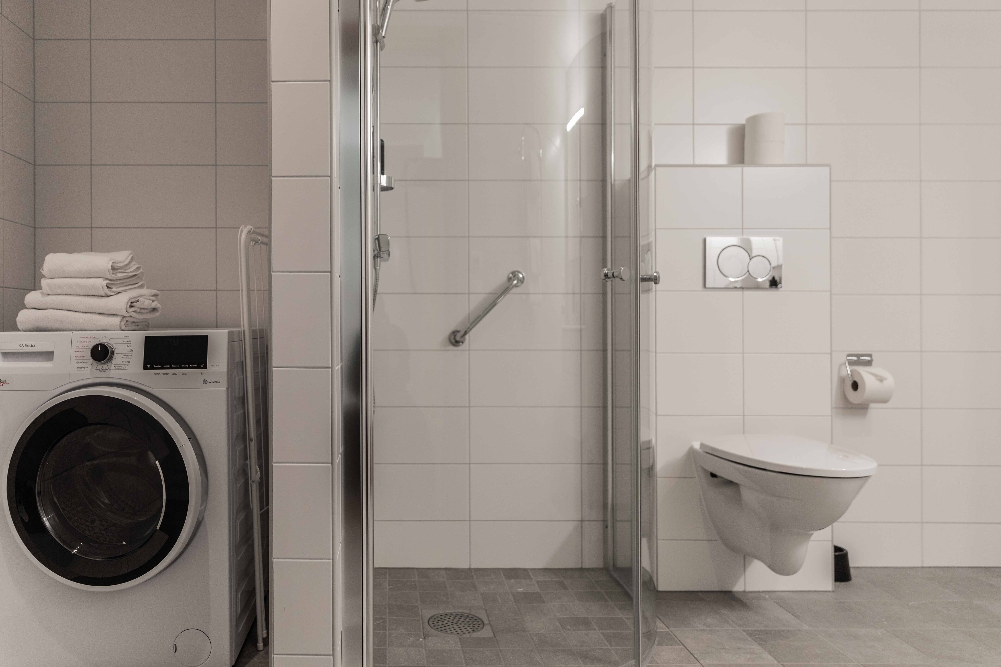A modern bathroom with a glass-enclosed shower, a toilet, and a washing machine.