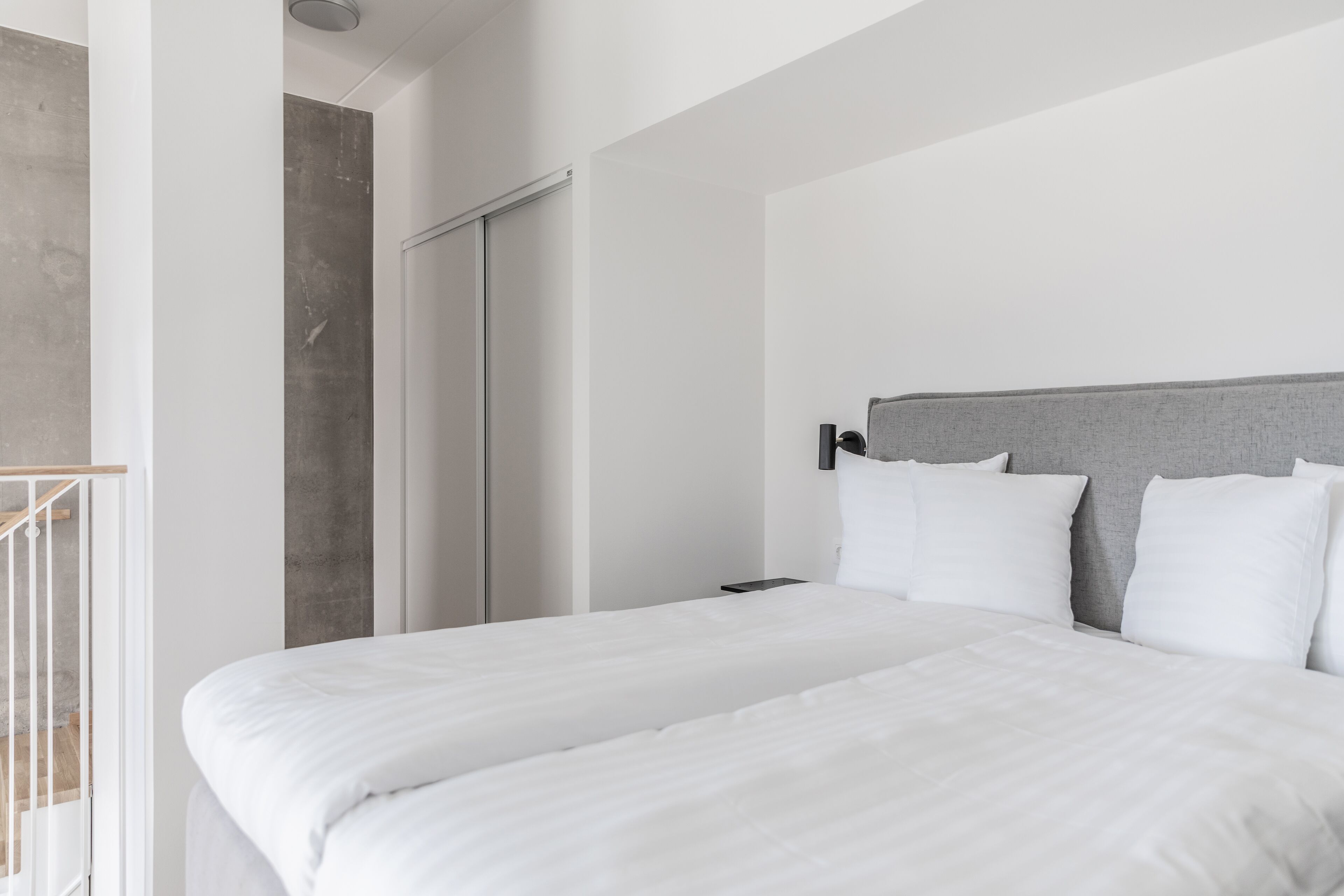 Una habitación de hotel moderna con una cama grande, un cabecero gris y una escalera de madera.