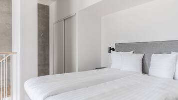 Una habitación de hotel moderna con una cama grande, un cabecero gris y una escalera de madera.