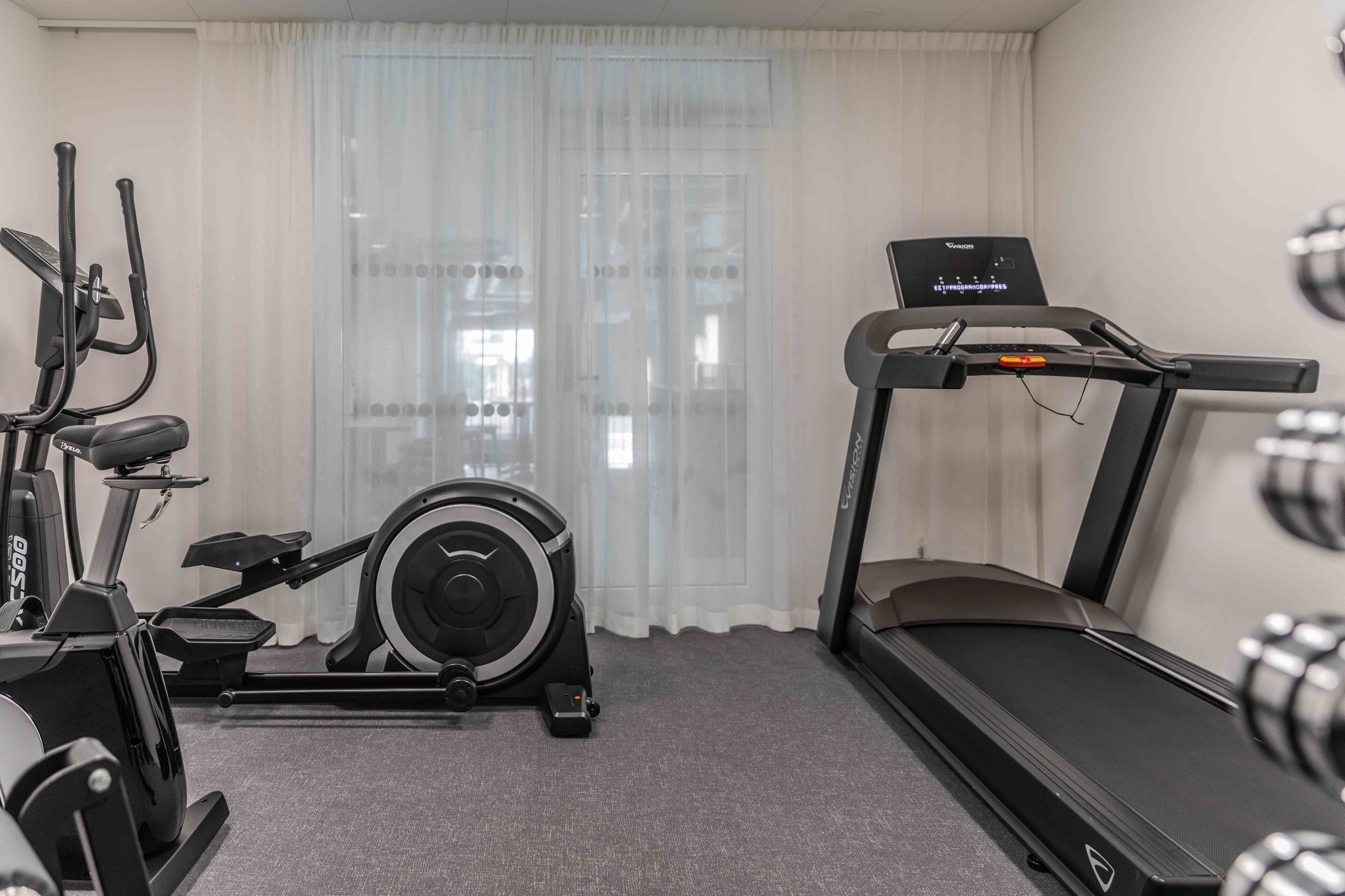 Een hotelkamer met een loopband, een elliptische machine en een hometrainer.