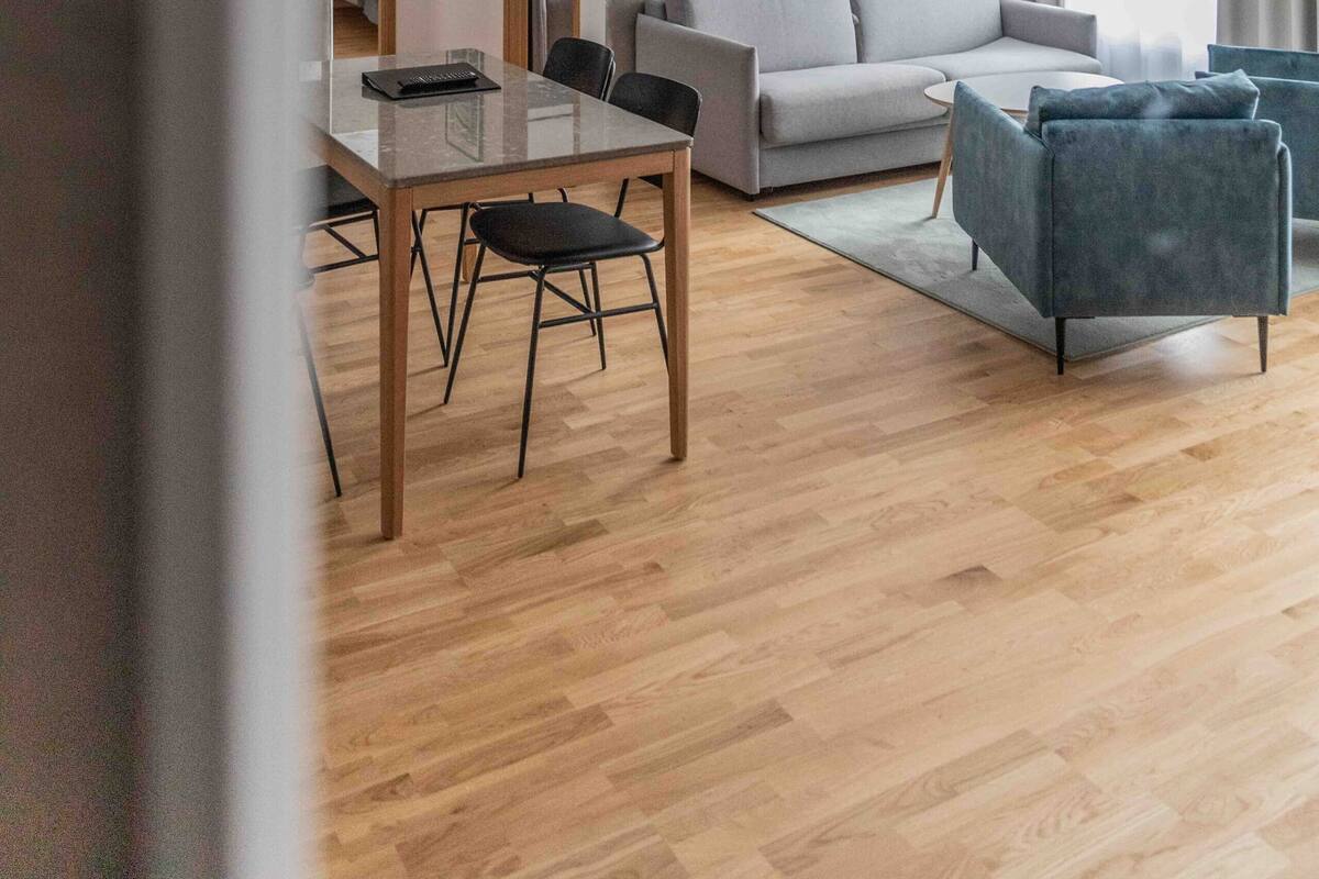 Een moderne woonkamer met een bank, twee fauteuils, een eettafel met stoelen en een groot raam met gordijnen.