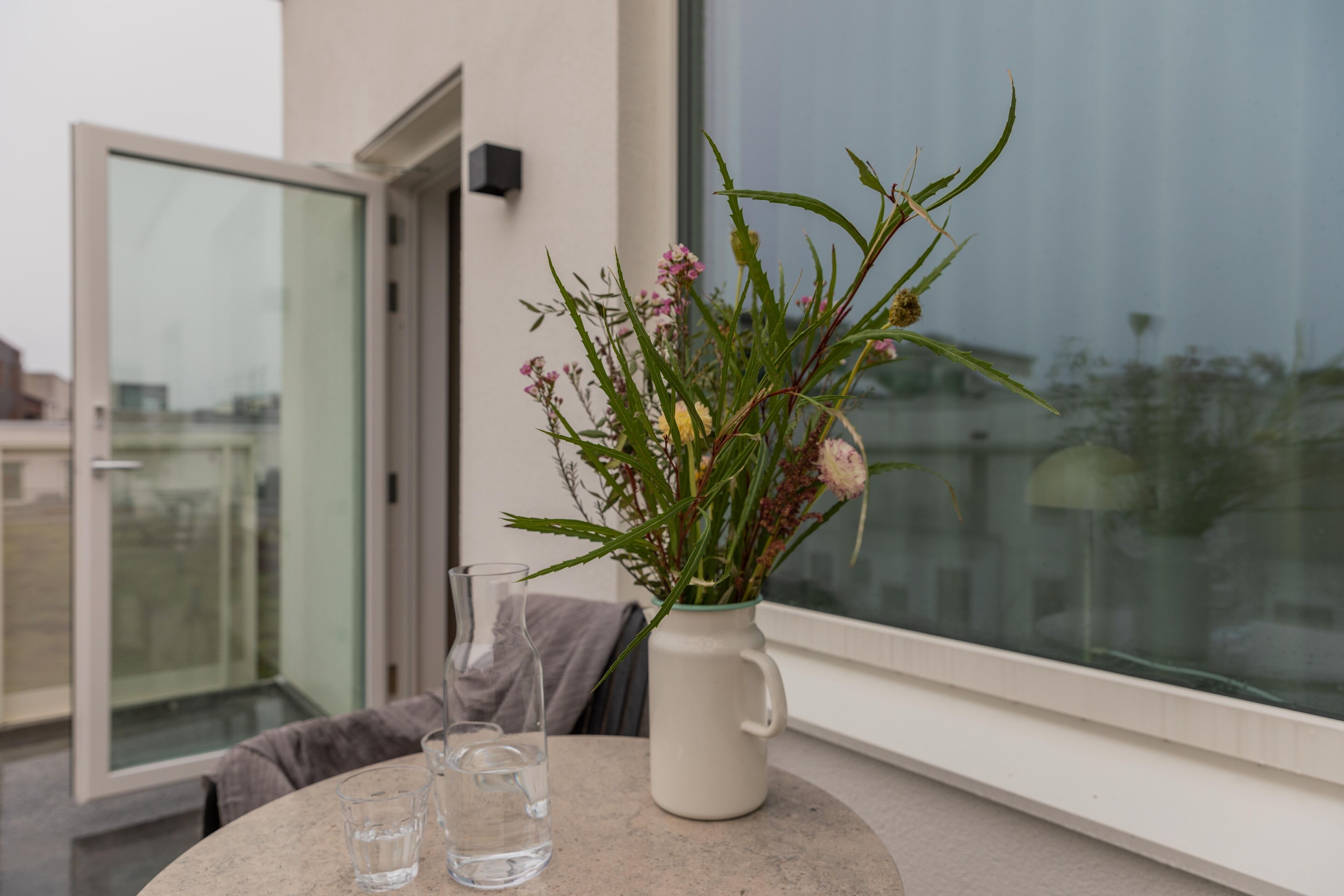 A balcony with a table, a vase with flowers, and a glass of water.