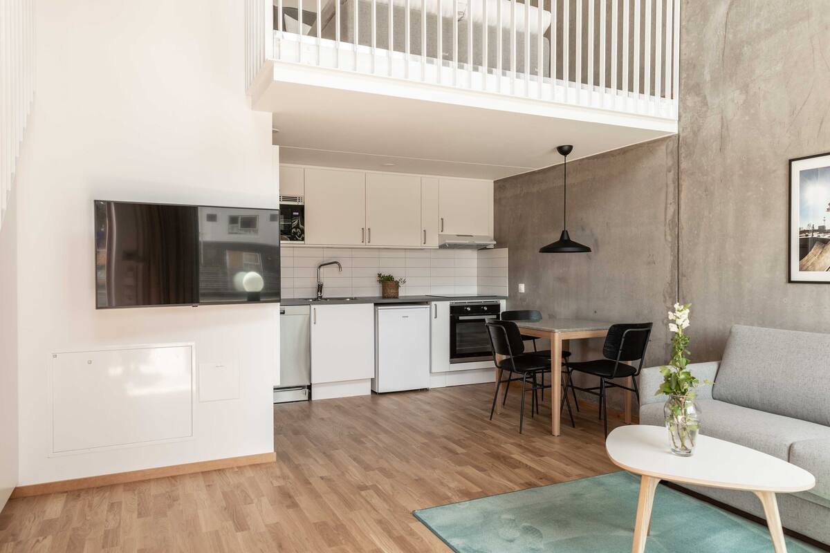 Een moderne keuken met witte kasten, een ingebouwde oven en een eethoek met een tafel en stoelen.