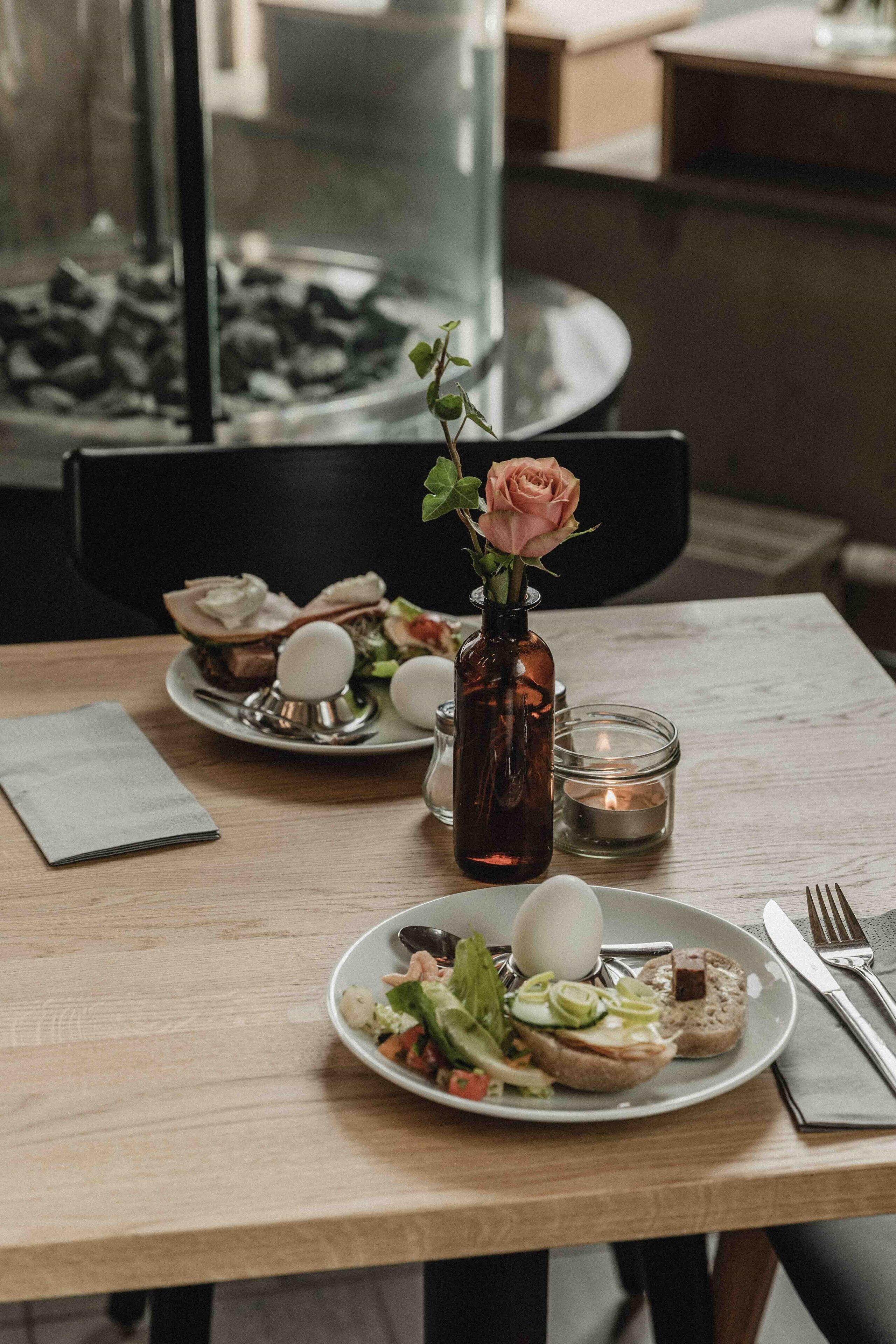 A dining table with plates of food, a vase with a flower, and a candle.