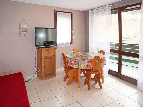 A room with a television on a wooden cabinet, a dining table with floral tablecloth, and a sliding glass door to the outside.