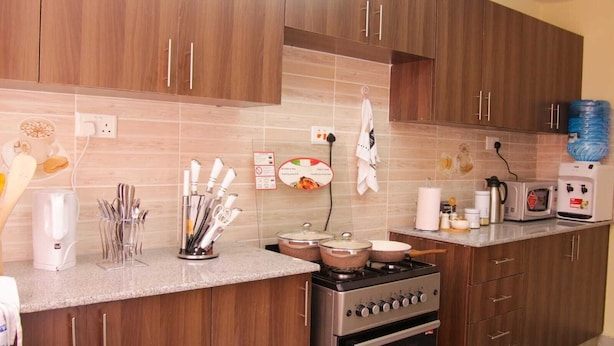 A modern kitchen with wooden cabinets, a gas stove, a microwave, and various kitchen utensils. - Stay.Plus Milimani Luxe Apartment (Kisumu)