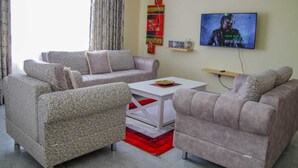 A living room with two sofas, a coffee table, and a TV on the wall. - Stay.Plus Milimani Luxe Apartment (Kisumu)