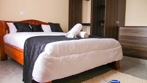 A neatly made bed with white and black bedding, a wooden headboard, and a dark wooden dresser with drawers. - Stay.Plus Milimani Luxe Apartment (Kisumu)