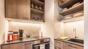 Une cuisine avec des meubles de rangement en bois, un four encastré, un évier et un plan de travail sur lequel se trouvent une machine à café et une bouilloire.