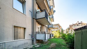 Un immeuble résidentiel à plusieurs étages, doté de balcons, d’un petit espace jardin et d’un coffret métallique pour les installations techniques.