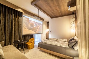 Une chambre moderne avec un lit, une petite table, une chaise et un grand écran affichant un paysage désertique.