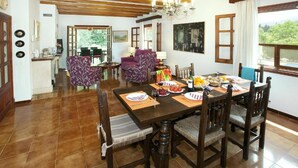 Un coin repas avec une table en bois dressée pour le repas, entourée de chaises, et une vue sur l’extérieur grâce à de grandes fenêtres.