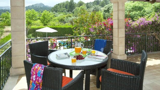 Un espace extérieur abrité, aménagé avec des chaises en osier, une table sur laquelle se trouve une boisson, et offrant une vue sur un jardin luxuriant.