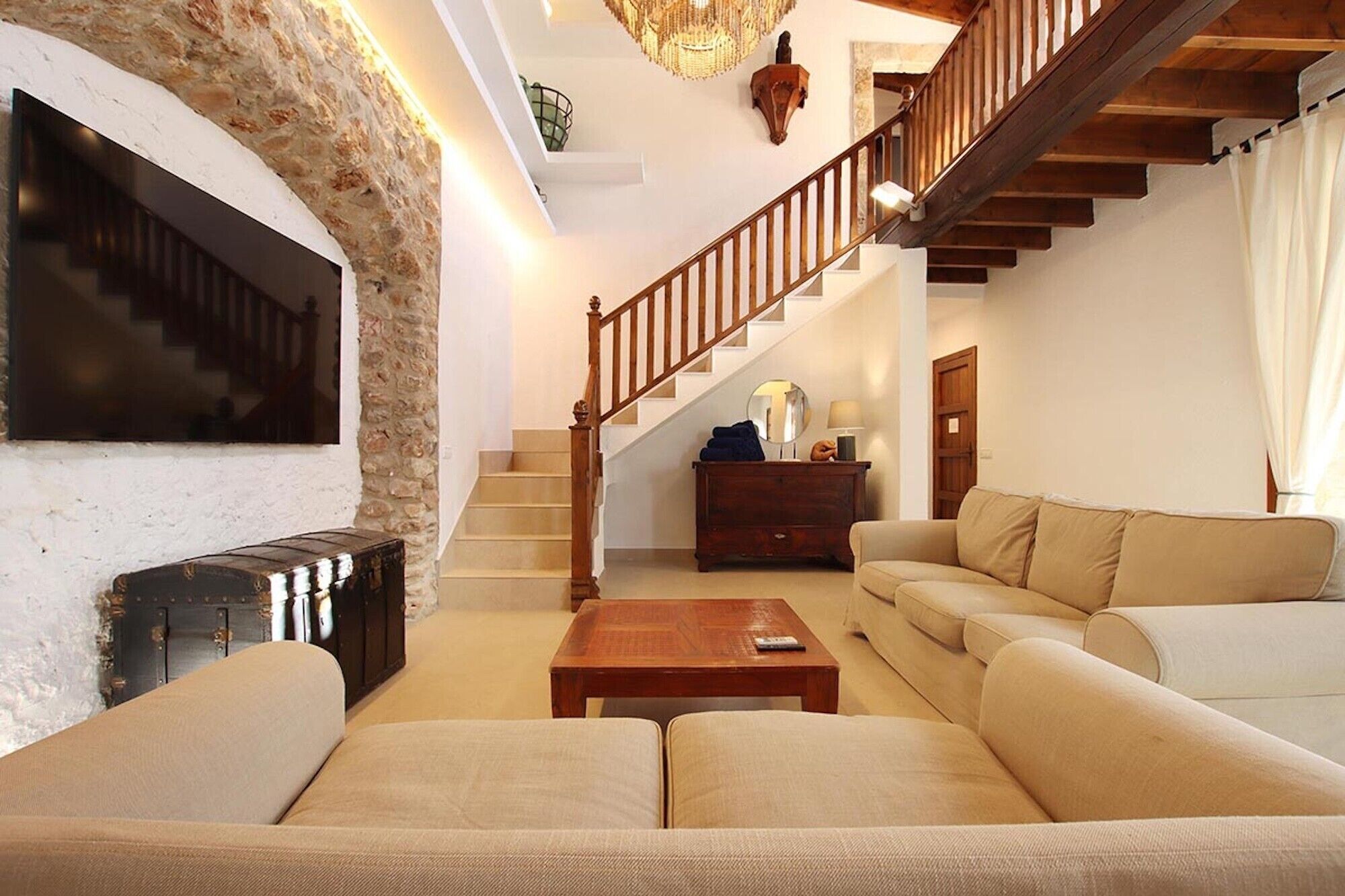 Una sala de estar con sofá, mesa de centro, chimenea, escalera y candelabro.