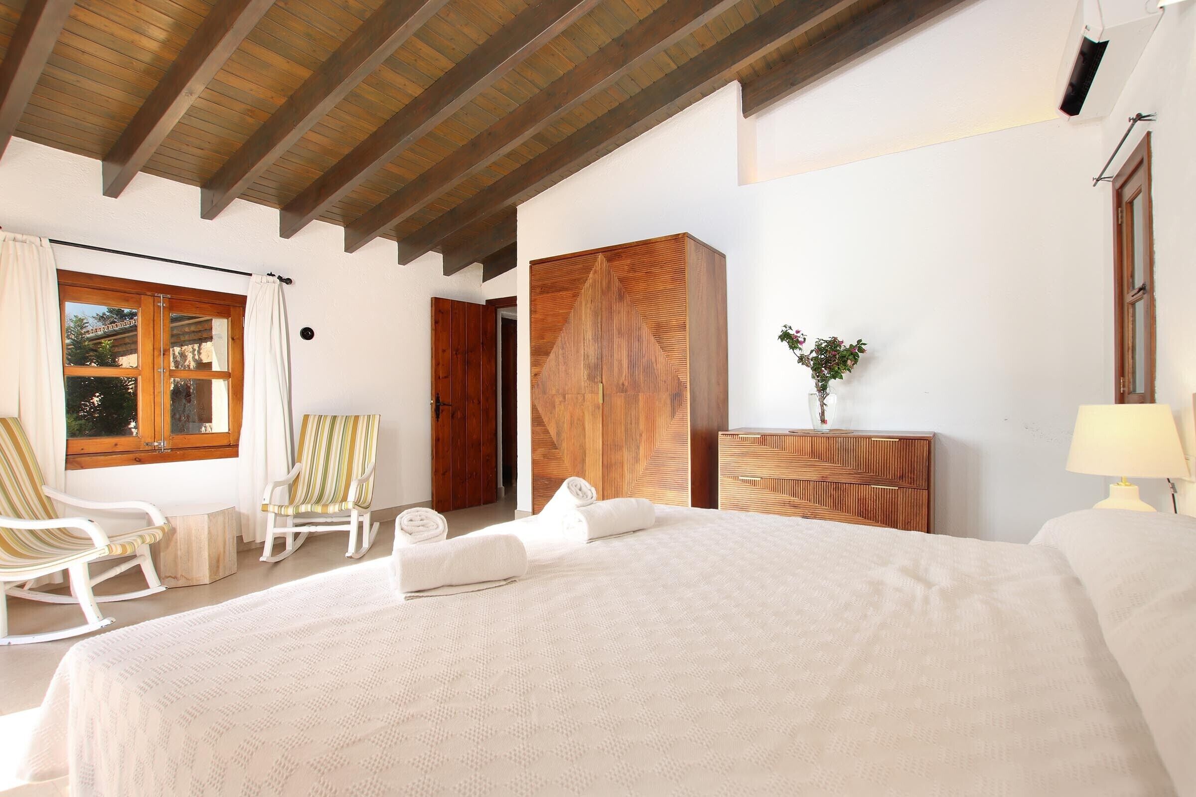 A bedroom with a large bed, wooden wardrobe, and a window with curtains.
