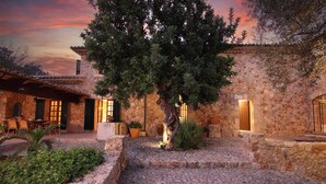 Un patio de piedra con un árbol, mobiliario exterior y un muro de piedra.