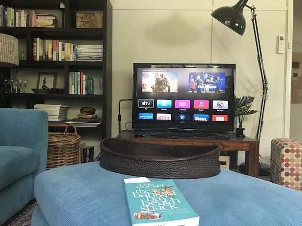 A living room with a television displaying various streaming services, a bookshelf, a lamp, and a book on a table.