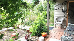 A covered patio with a wooden deck, potted plants, a wicker chair, and a bicycle. - Loves Road Retreat   (Barwon Downs)