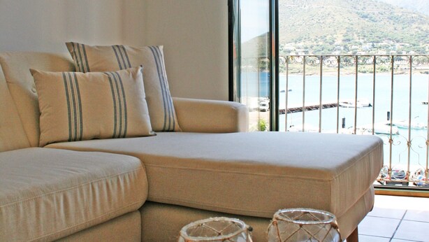 A room with a sofa, a coffee table with decorative items, a large window with a view of a body of water and hills. - Pet-Friendly Apartment with Sea View, Balconies & A/C (El Port de la Selva)