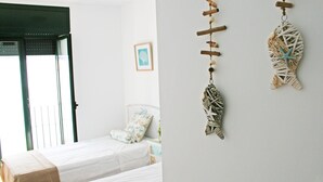 A bedroom with two beds, a window with a view, and wall decorations including a fish ornament. - Pet-Friendly Apartment with Sea View, Balconies & A/C (El Port de la Selva)