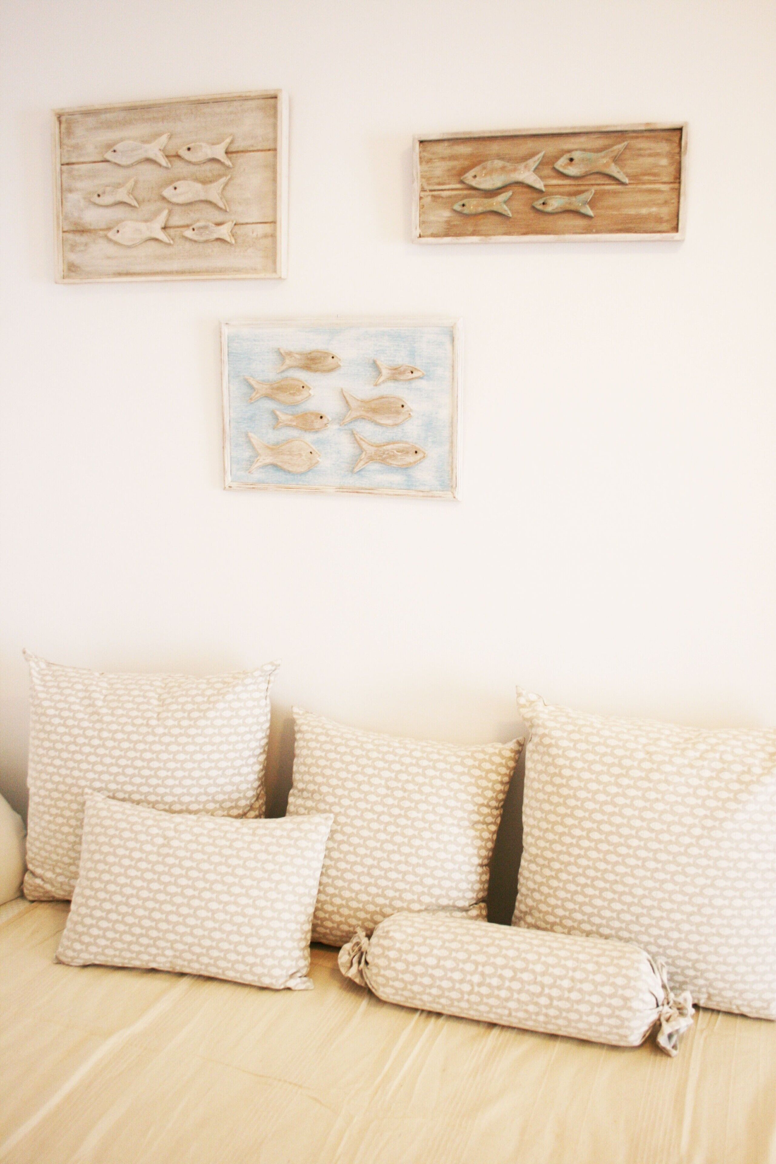 Una stanza con pavimento in legno, un divano beige con cuscini decorati e tre opere d'arte a tema pesciolicini appese al muro.