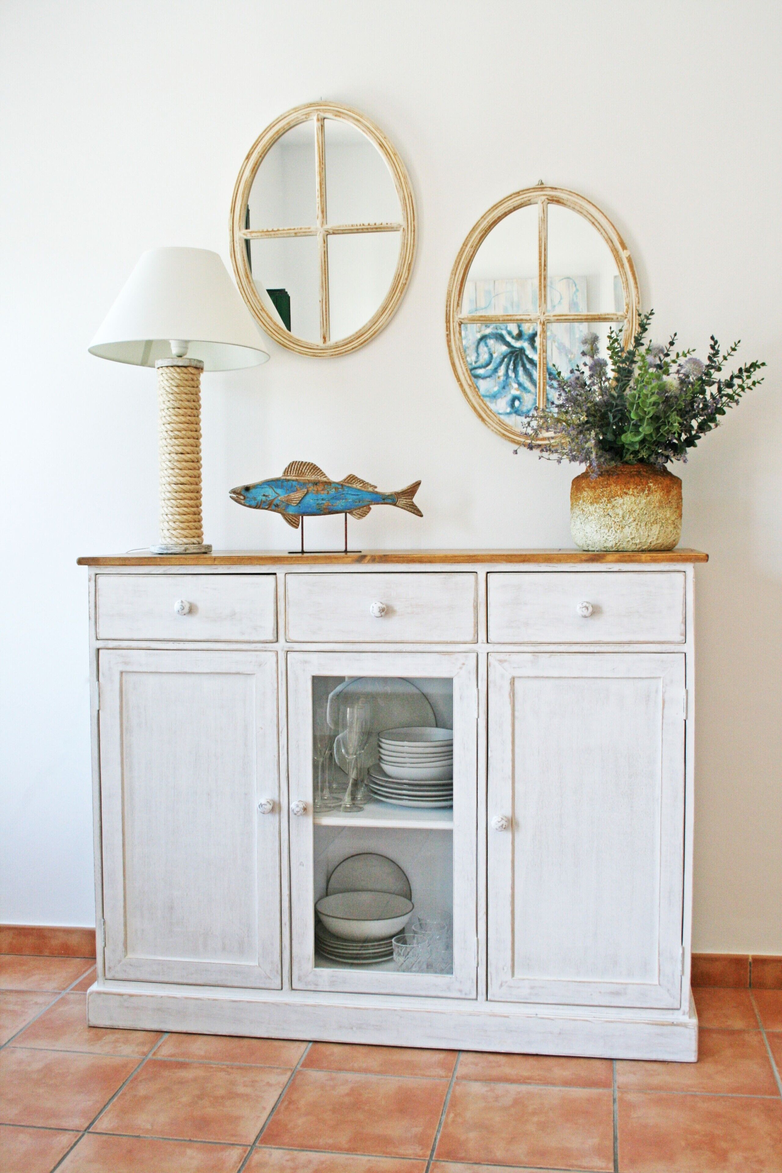A white cabinet with two round mirrors, a lamp, and a decorative fish.