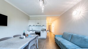 A modern kitchen with white cabinets, a dining table with chairs, a blue sofa, and a wall-mounted light fixture. - Lo Scorcio sul Lago (Salò)