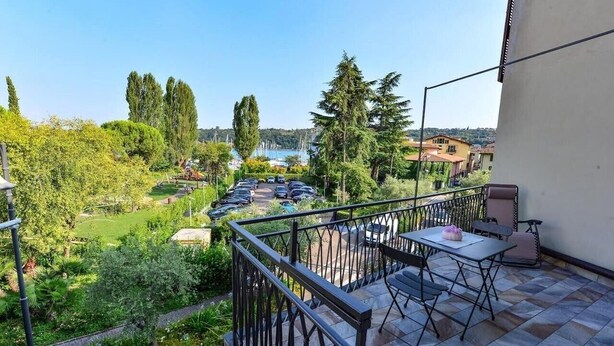 A balcony with a view of a marina and greenery, a table with chairs, and a railing. - Lo Scorcio sul Lago (Salò)