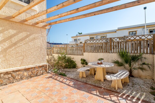 A patio with a tiled floor, wooden furniture, and a view of a building with balconies.