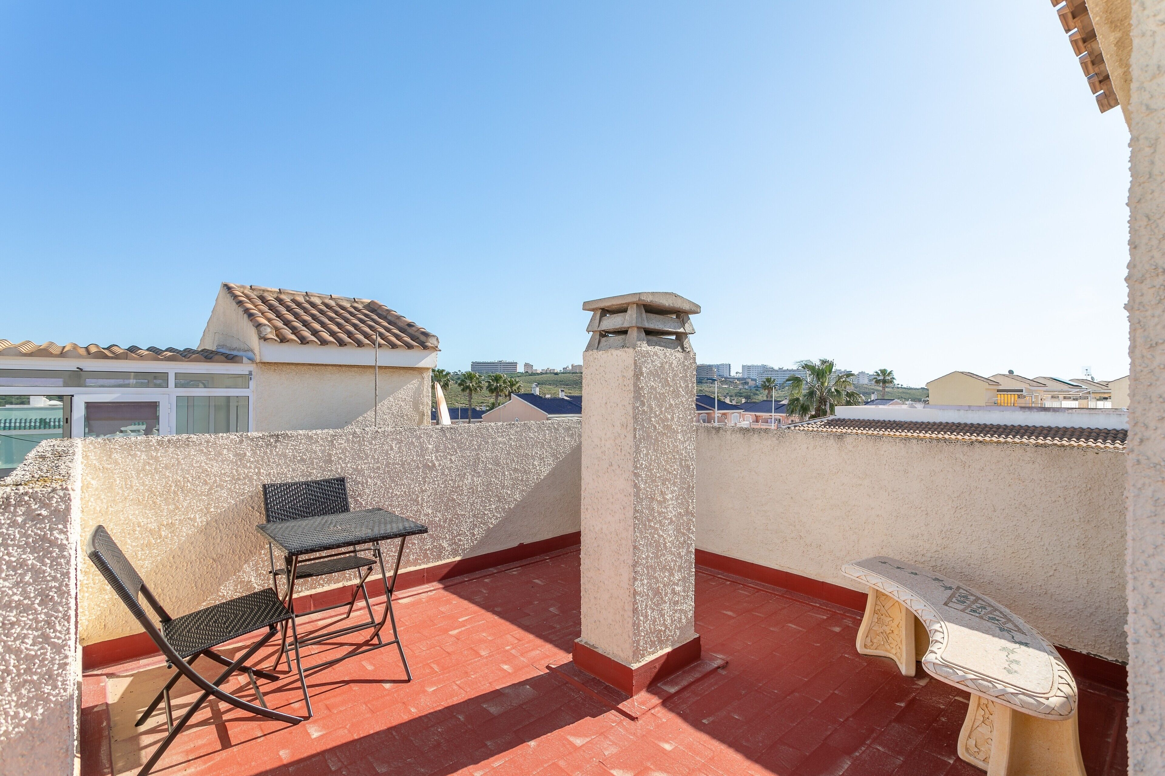 A balcony with a table and chairs, a stone pillar, and a view of the cityscape.