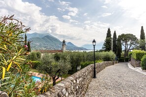 Un chemin de pierres menant à une piscine, entouré de verdure et offrant une vue sur les montagnes.