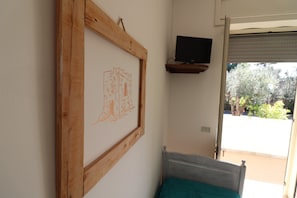 A room with a bed, a TV mounted on a wall, and a window with a view of greenery outside.