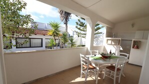 Un balcon avec une table et des chaises, une vue sur le quartier et une porte donnant sur une pièce.