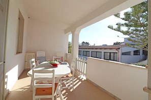 A balcony with a white table and chairs, a potted plant, and a view of buildings and trees.