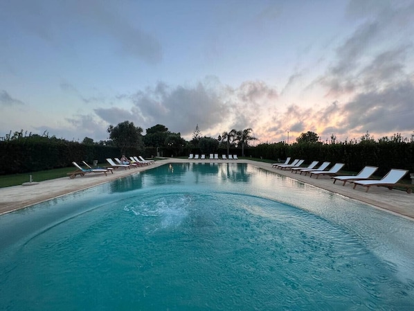 A swimming pool with lounge chairs and a hedge-lined border.