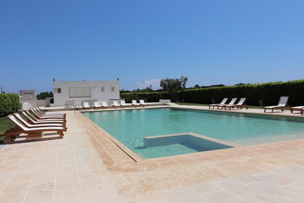 Une piscine rectangulaire avec une terrasse carrelée, entourée de chaises longues.
