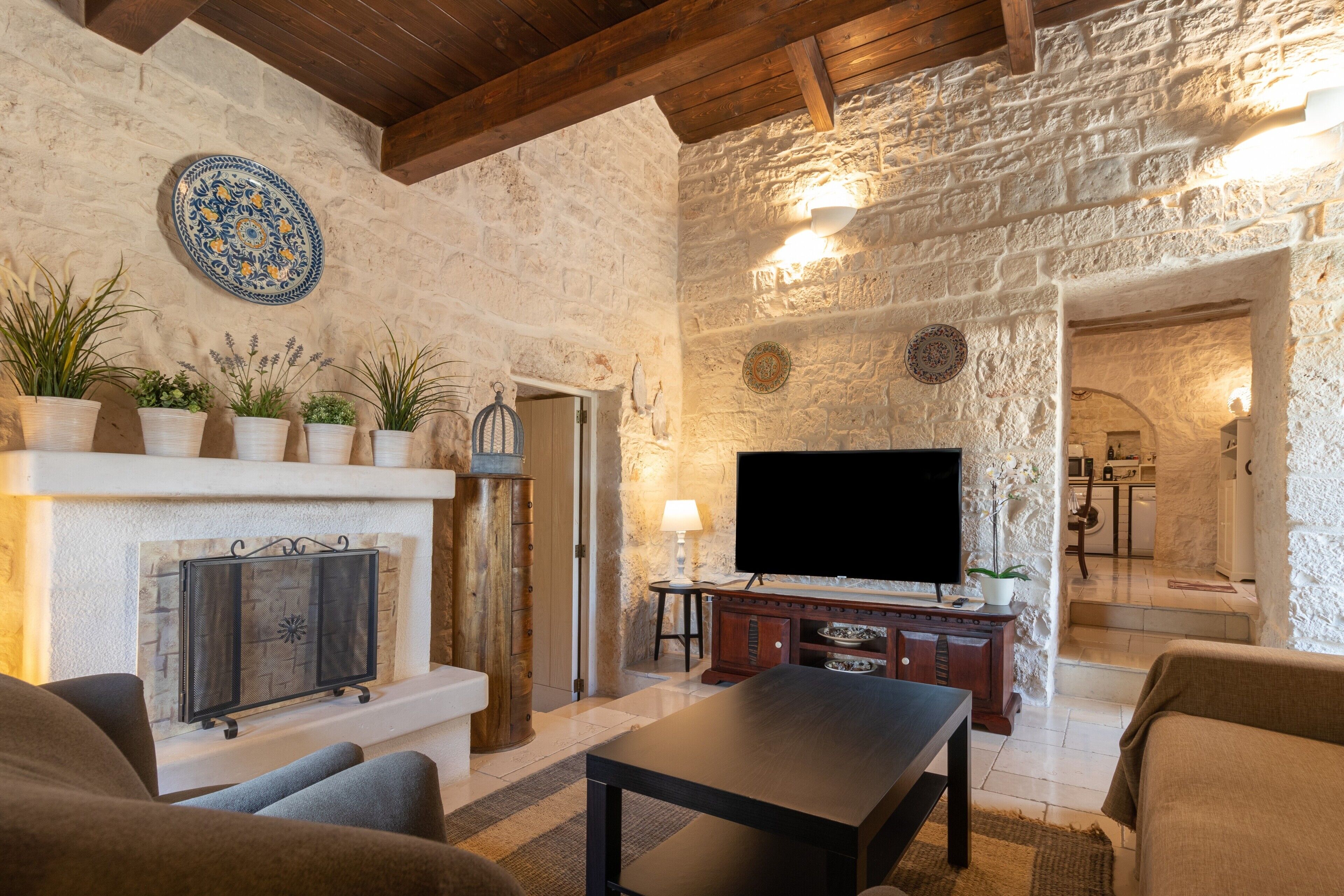 A stone-walled living room with a fireplace, a flat-screen TV, and a sofa.