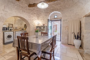 Une cuisine aux murs de pierre, avec une table à manger, des chaises et un lave-linge.