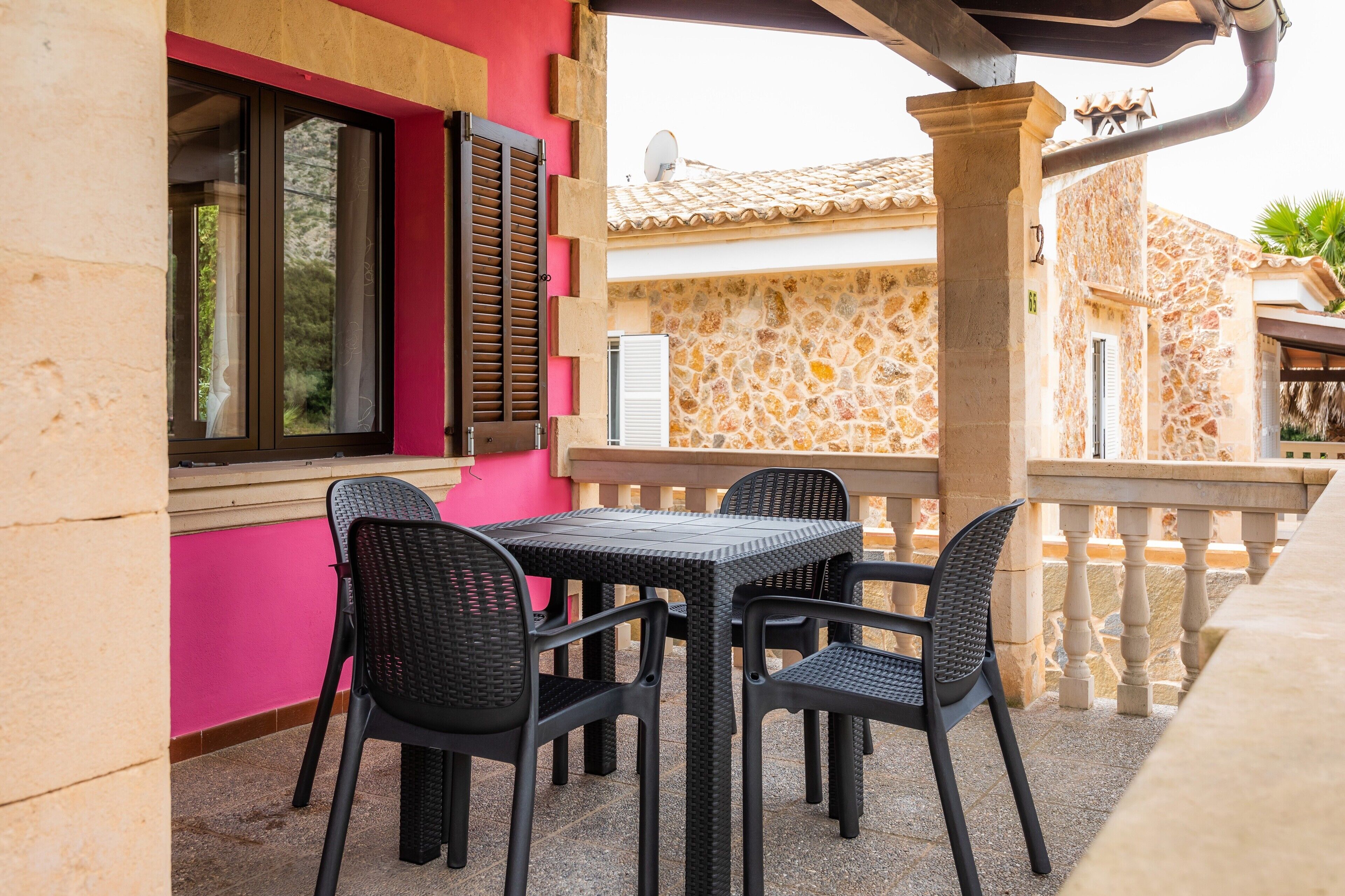 A patio with a table and chairs, a window with shutters, and a stone wall.