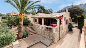 Une petite maison avec une façade en pierre, un balcon et un palmier dans le jardin.