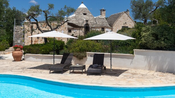 A pool area with lounge chairs and umbrellas, a stone building in the background, and a clear blue sky. - Holiday Home Trullo Nurillo with Pool & Wi-Fi (Alberobello)
