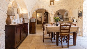 A rustic stone interior with a dining table, chairs, and a kitchen area. - Holiday Home Trullo Nurillo with Pool & Wi-Fi (Alberobello)