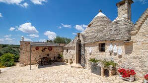 A stone house with a tiled roof, a small patio with a table and chairs, and potted plants. - Holiday Home Trullo Nurillo with Pool & Wi-Fi (Alberobello)