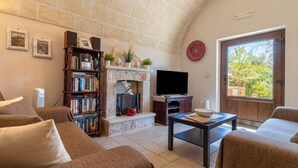A living room with a stone fireplace, a bookshelf, a television, and a view through a door. - Holiday Home Trullo Nurillo with Pool & Wi-Fi (Alberobello)
