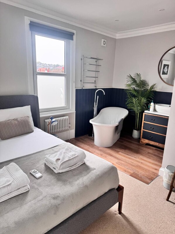Un dormitorio con cama, radiador, ventana, lavamanos, espejo, planta y cómoda.