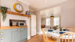 Una cocina compacta con microondas, refrigerador y una estantería de madera con libros y un reloj.
