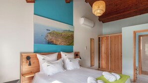 A bedroom with a bed, a painting of a coastal landscape, a wooden wardrobe, and a green bedspread.