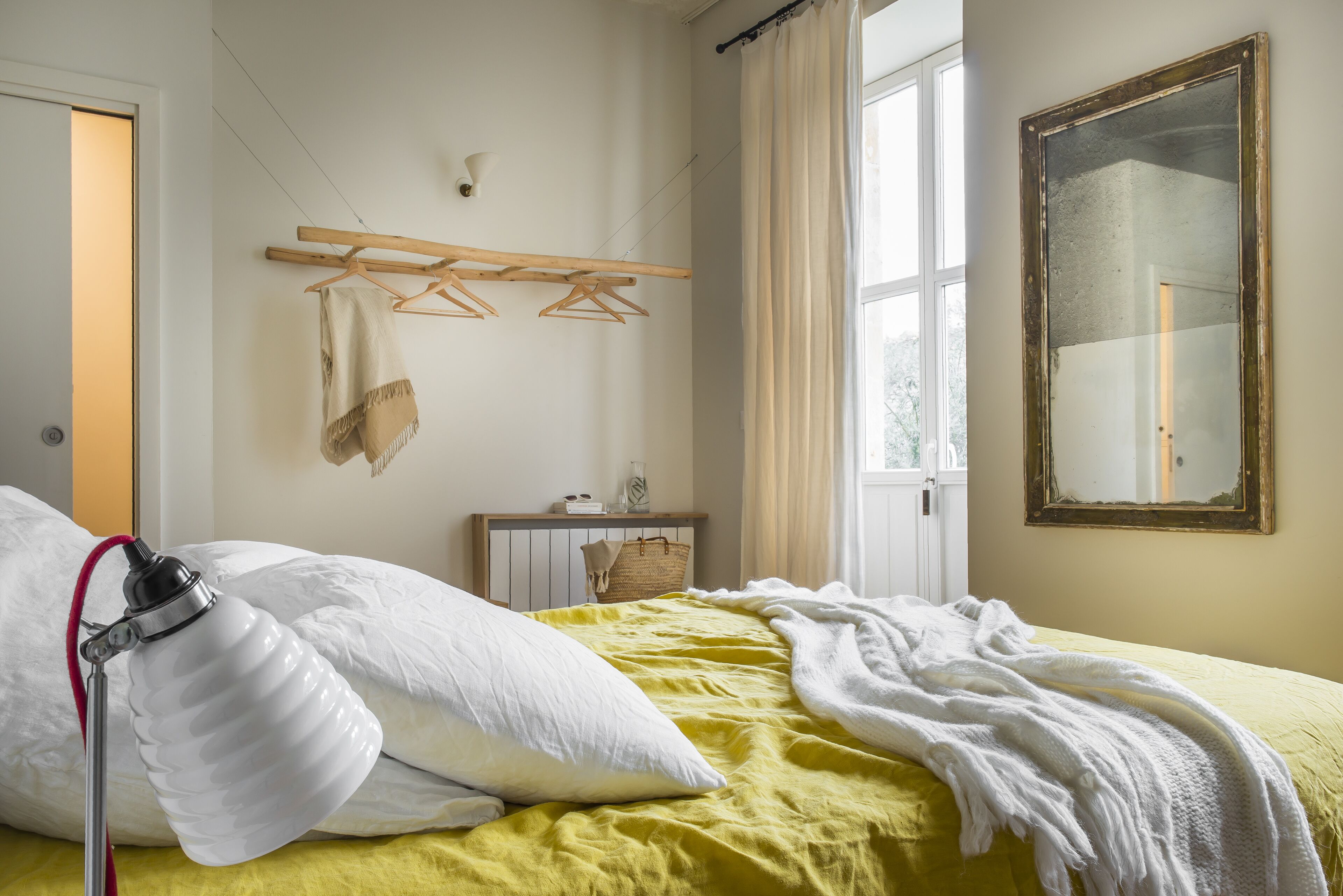 A hotel room with a bed, a bedside table, a mirror, and a window with curtains.